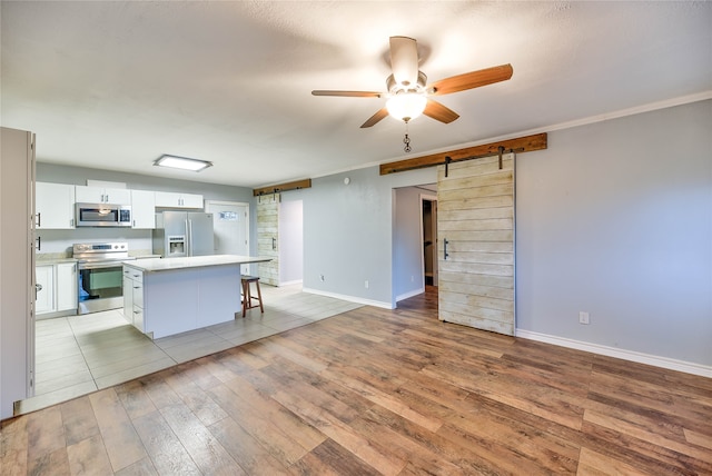 kitchen featuring a breakfast bar, appliances with stainless steel finishes, a barn door, a center island, and ceiling fan