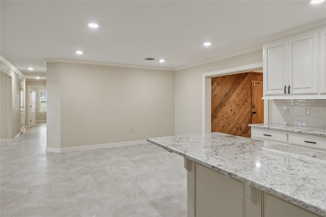 kitchen with backsplash, ornamental molding, white cabinets, and light stone countertops