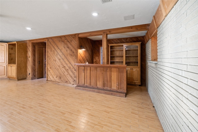 empty room featuring wooden walls, a textured ceiling, brick wall, and light hardwood / wood-style floors