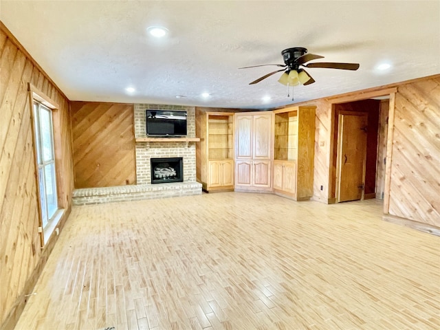 unfurnished living room with wood walls, light hardwood / wood-style floors, a fireplace, and ceiling fan