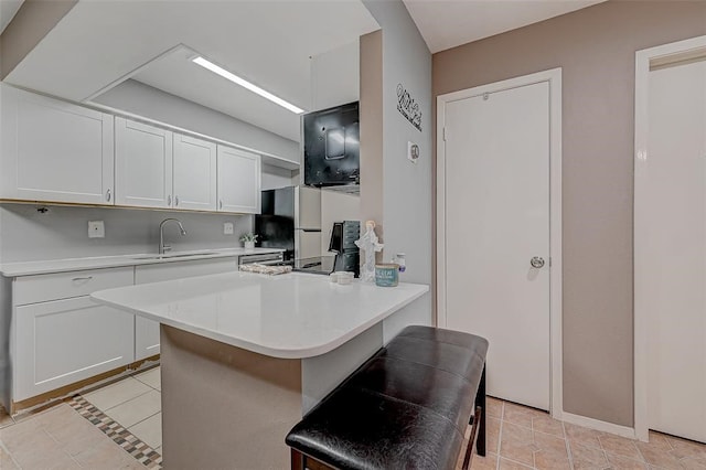 kitchen with white cabinets, a kitchen bar, sink, and light tile floors