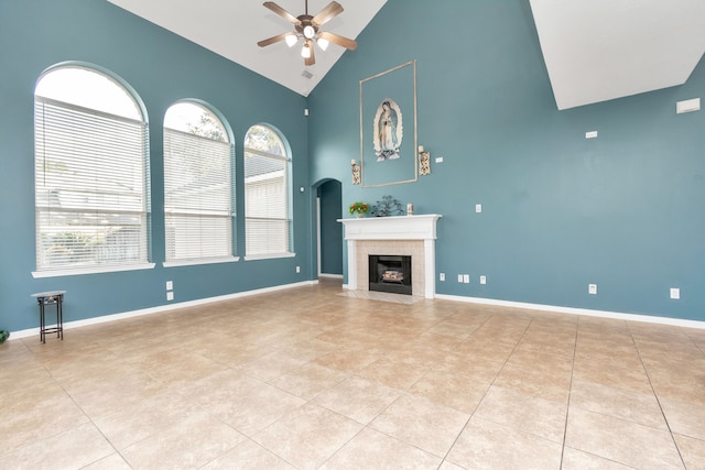 unfurnished living room featuring ceiling fan, a tile fireplace, high vaulted ceiling, and a healthy amount of sunlight