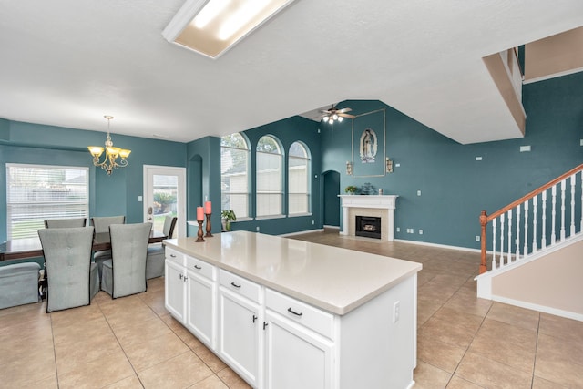 kitchen featuring a center island, light tile floors, ceiling fan with notable chandelier, decorative light fixtures, and white cabinets