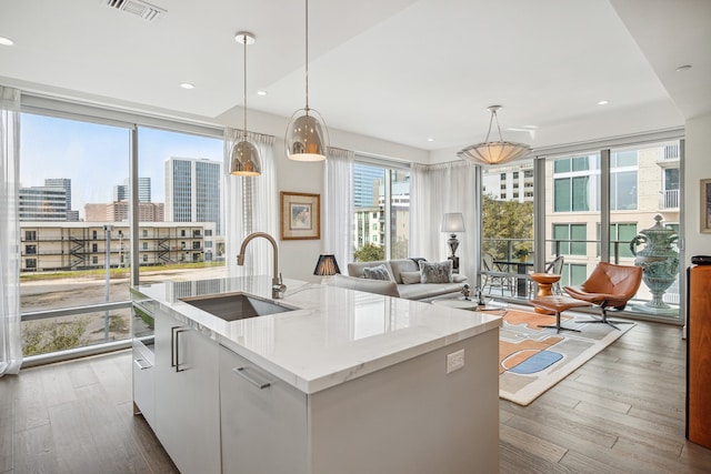 kitchen with pendant lighting, hardwood / wood-style flooring, white cabinets, a kitchen island with sink, and sink