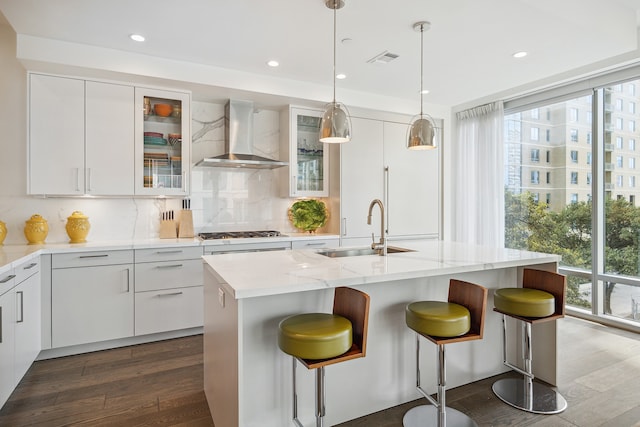 kitchen with backsplash, wall chimney exhaust hood, a center island with sink, and white cabinetry