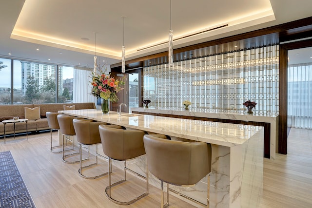 bar with decorative light fixtures, light stone counters, a tray ceiling, and a wall of windows