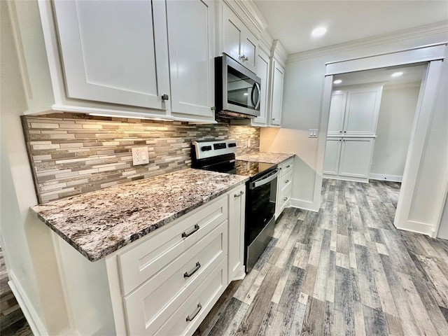 kitchen with appliances with stainless steel finishes, white cabinets, crown molding, light hardwood / wood-style flooring, and backsplash