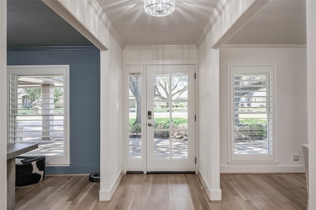 doorway to outside with light hardwood / wood-style flooring, crown molding, a notable chandelier, and a healthy amount of sunlight