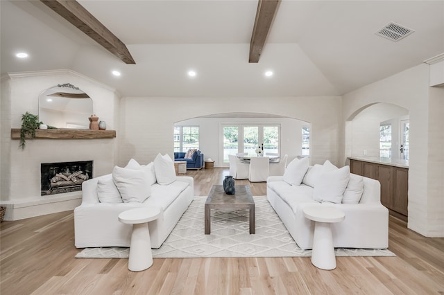 living room featuring a large fireplace, french doors, vaulted ceiling with beams, and light hardwood / wood-style flooring