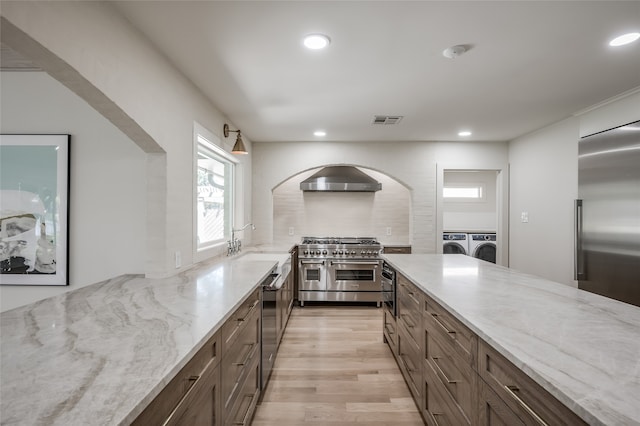 kitchen featuring premium appliances, washing machine and dryer, light stone counters, and light wood-type flooring