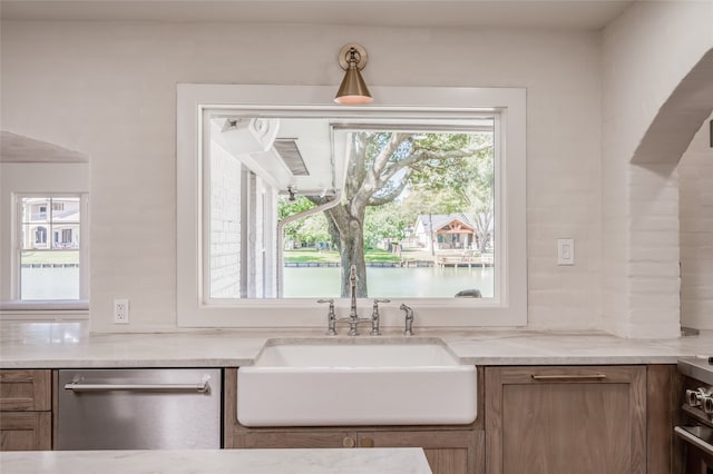 kitchen featuring appliances with stainless steel finishes, light stone countertops, sink, and a water view