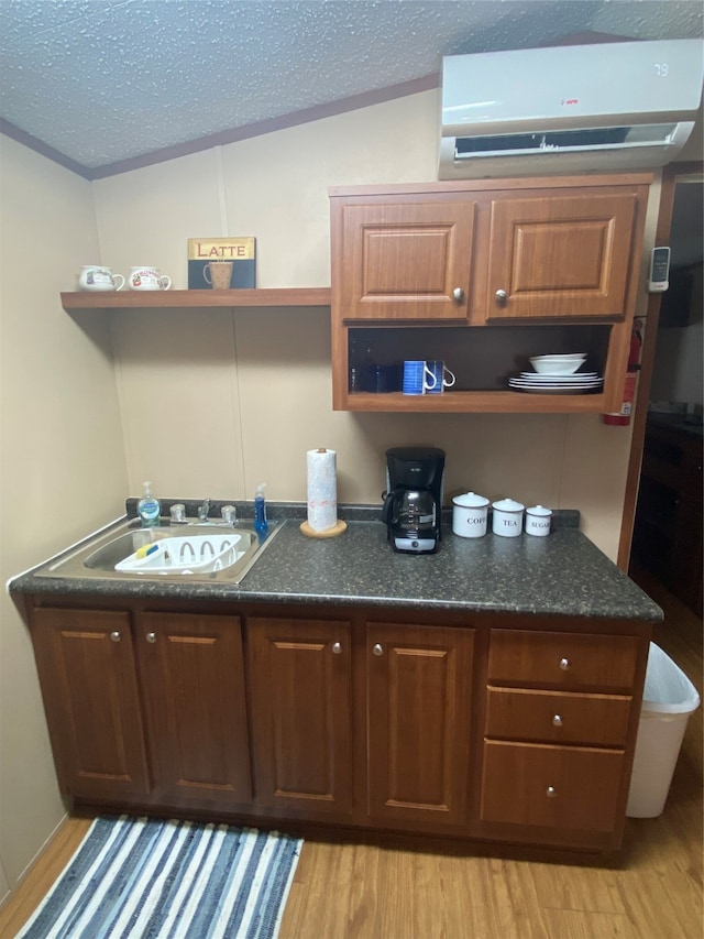 kitchen featuring sink, a wall mounted air conditioner, light hardwood / wood-style floors, a textured ceiling, and lofted ceiling