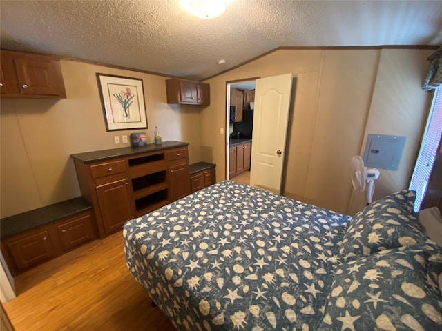 bedroom with lofted ceiling, a textured ceiling, connected bathroom, and light wood-type flooring