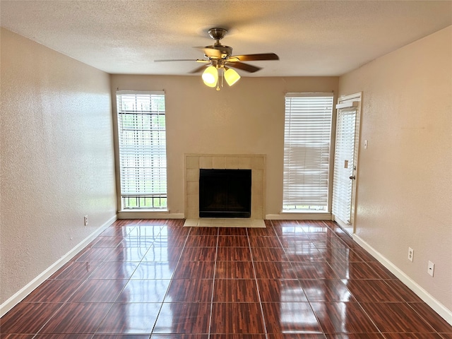 unfurnished living room with dark tile flooring, a healthy amount of sunlight, ceiling fan, and a tile fireplace