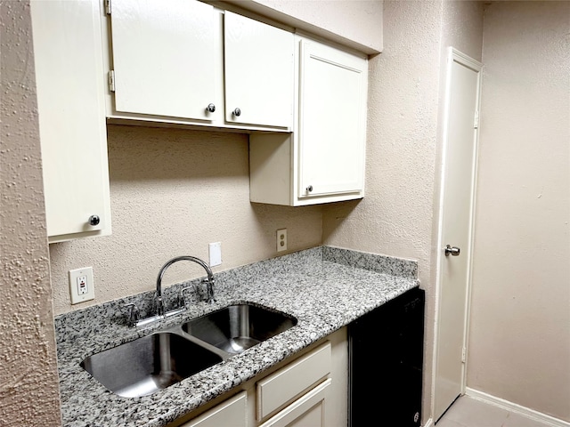 kitchen featuring black dishwasher, white cabinets, light stone counters, and sink