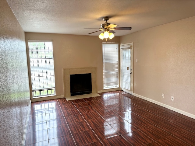 unfurnished living room featuring a tile fireplace, ceiling fan, a textured ceiling, and dark tile flooring