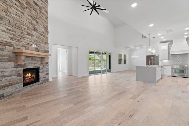 unfurnished living room with a stone fireplace, light hardwood / wood-style floors, sink, and a high ceiling