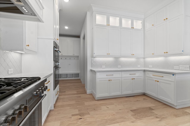 kitchen with appliances with stainless steel finishes, white cabinets, light wood-type flooring, and backsplash