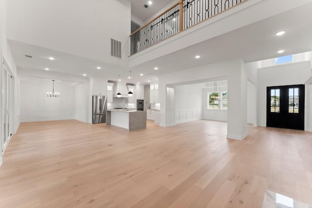 unfurnished living room featuring a towering ceiling, a chandelier, sink, and light wood-type flooring