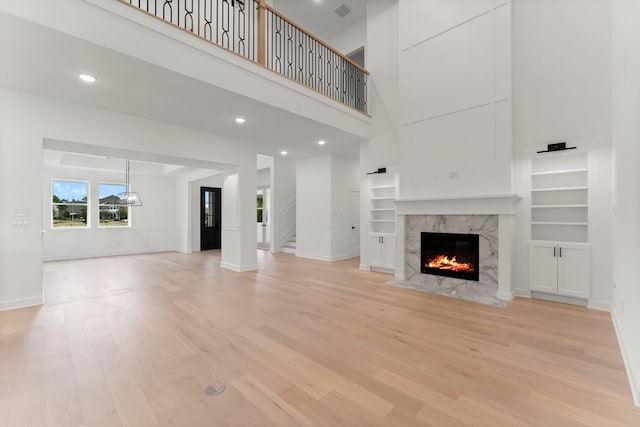 unfurnished living room with built in features, a premium fireplace, a high ceiling, and light wood-type flooring