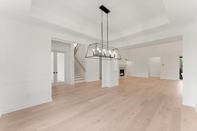 unfurnished dining area with crown molding, a raised ceiling, french doors, and light wood-type flooring