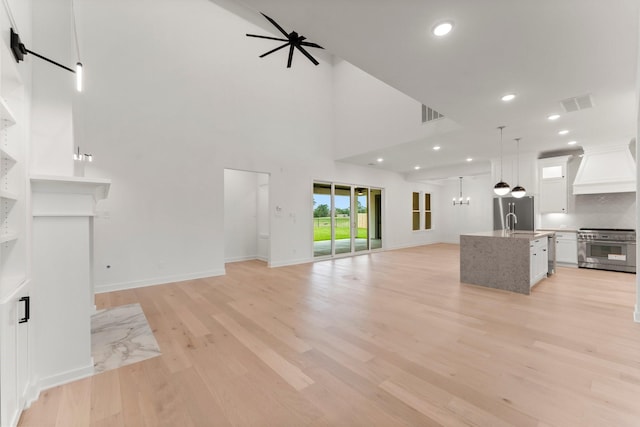 unfurnished living room with sink, ceiling fan with notable chandelier, light hardwood / wood-style floors, and a towering ceiling