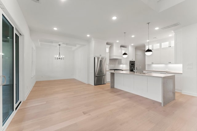 kitchen featuring white cabinetry, decorative light fixtures, stainless steel appliances, and an island with sink