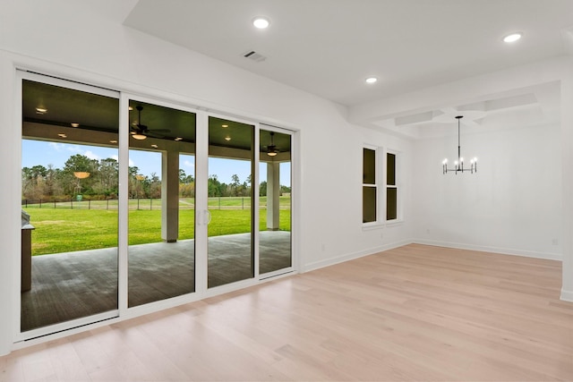 empty room featuring ceiling fan with notable chandelier and light hardwood / wood-style flooring