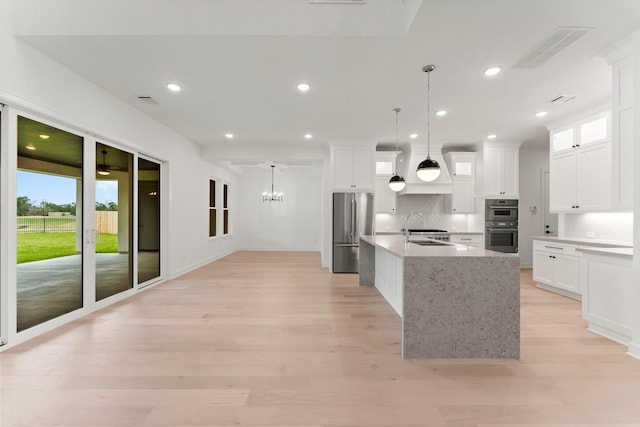 kitchen featuring white cabinetry, hanging light fixtures, stainless steel appliances, and a center island with sink