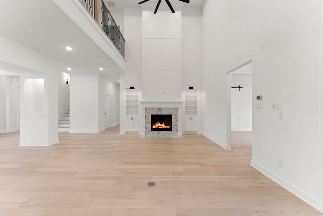 unfurnished living room featuring a fireplace, light hardwood / wood-style floors, ceiling fan, and a high ceiling