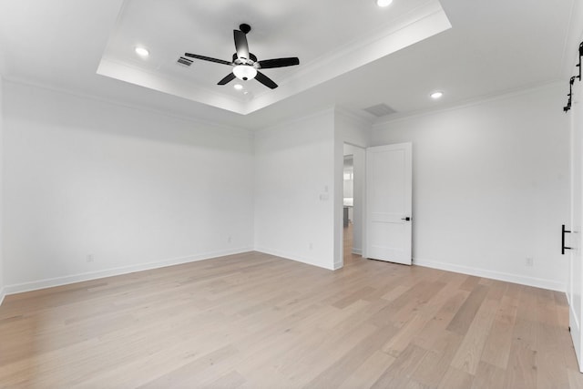 spare room featuring light hardwood / wood-style flooring, ornamental molding, a raised ceiling, ceiling fan, and a barn door