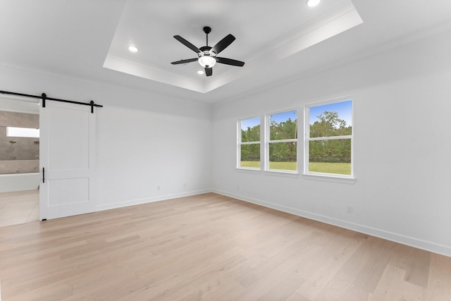 unfurnished room featuring ceiling fan, a barn door, light hardwood / wood-style floors, and a tray ceiling