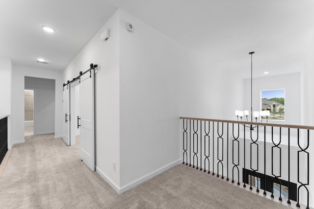 hall featuring an inviting chandelier, light colored carpet, and a barn door