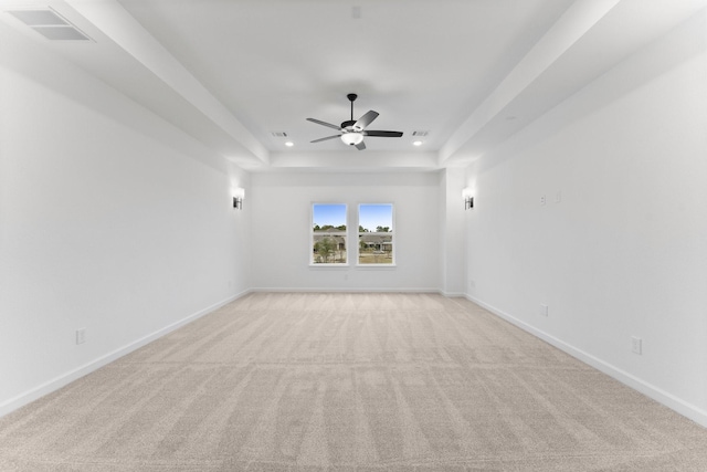 carpeted spare room with a raised ceiling and ceiling fan