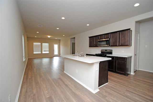 kitchen with an island with sink, light hardwood / wood-style flooring, appliances with stainless steel finishes, dark brown cabinetry, and sink