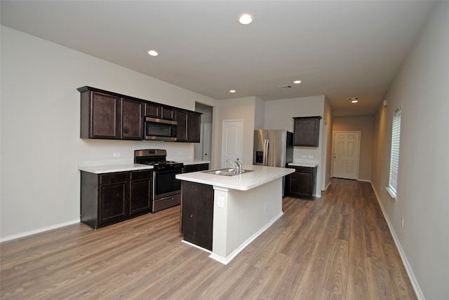 kitchen featuring appliances with stainless steel finishes, dark brown cabinets, light hardwood / wood-style flooring, a kitchen island with sink, and sink