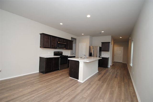 kitchen featuring appliances with stainless steel finishes, light wood-type flooring, an island with sink, sink, and dark brown cabinetry