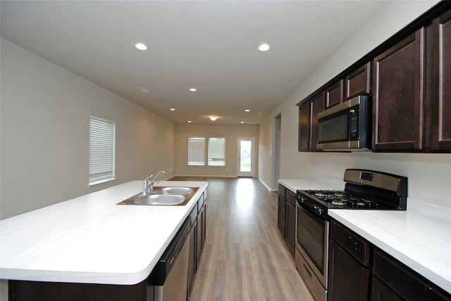 kitchen featuring light wood-type flooring, stainless steel appliances, sink, dark brown cabinetry, and a kitchen island with sink