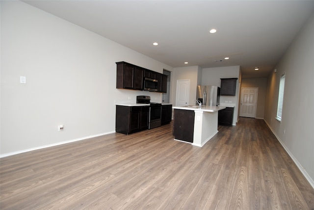 kitchen with an island with sink, stainless steel appliances, sink, dark brown cabinetry, and light hardwood / wood-style flooring