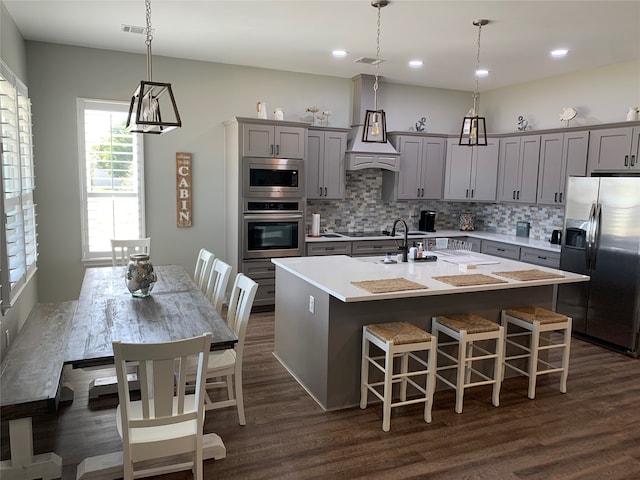 kitchen with pendant lighting, tasteful backsplash, a kitchen island with sink, and appliances with stainless steel finishes