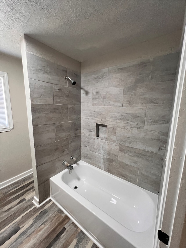 bathroom with a textured ceiling, tiled shower / bath combo, and wood-type flooring