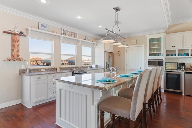 kitchen featuring white cabinets, an island with sink, a breakfast bar, decorative light fixtures, and stainless steel appliances