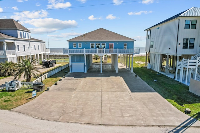 beach home featuring a carport, driveway, a front lawn, and a water view