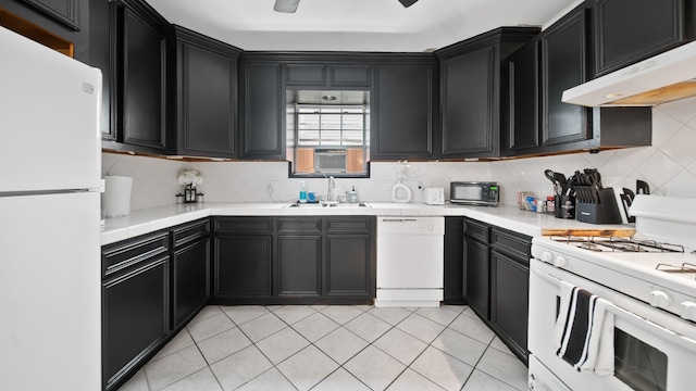 kitchen featuring under cabinet range hood, white appliances, dark cabinetry, and a sink