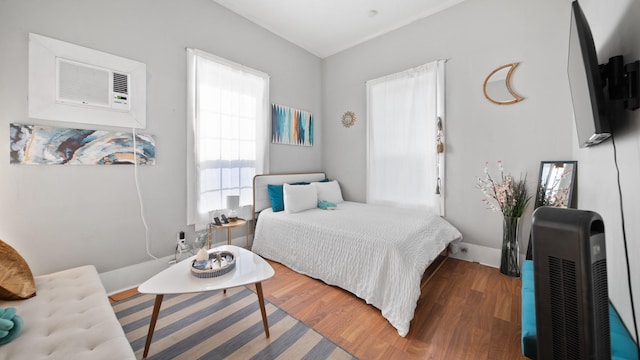 bedroom with heating unit, wood finished floors, baseboards, and a wall mounted air conditioner