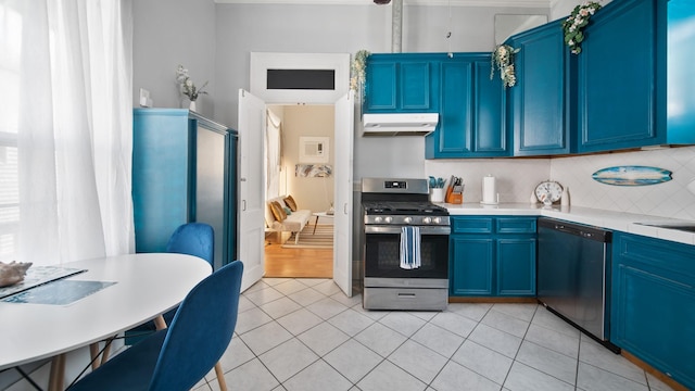 kitchen with under cabinet range hood, blue cabinetry, stainless steel appliances, light tile patterned flooring, and decorative backsplash