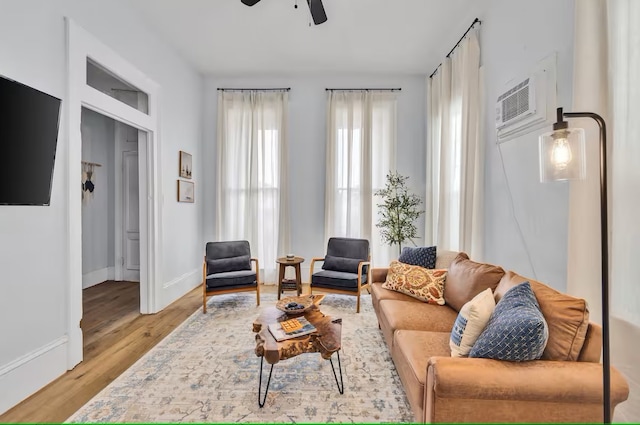 living room featuring a wall unit AC, a ceiling fan, light wood-type flooring, and baseboards