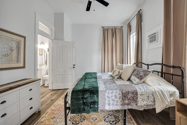 bedroom featuring ensuite bathroom, wood finished floors, arched walkways, a wall mounted AC, and a ceiling fan