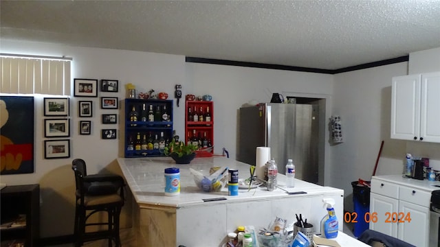 kitchen with stainless steel fridge, tile countertops, a textured ceiling, ornamental molding, and white cabinets