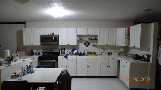 kitchen with white cabinets, range, sink, and a textured ceiling